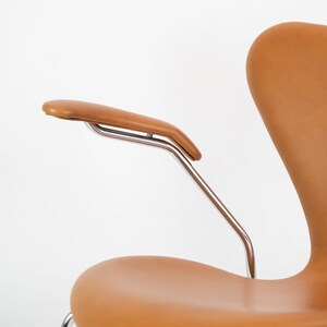 Puede incluir: Una silla de cuero marr&oacute;n con un marco cromado y un solo reposabrazos. La silla tiene un respaldo curvo y un asiento redondeado.