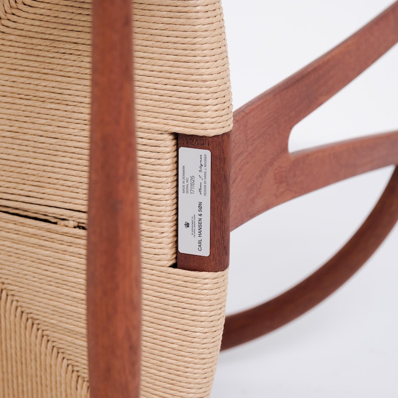May include: Close-up of a wooden rocking chair with woven seat and back. The chair has a light brown woven seat and back, with dark brown wooden frame. A label on the chair reads "CARL HANSEN & S&Oslash;N".