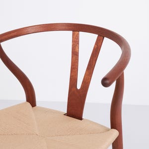 May include: Close-up of a wooden chair with a curved back and woven seat. The chair's frame is a rich brown color, and the seat is a light beige. The back of the chair has a distinctive Y-shaped design.