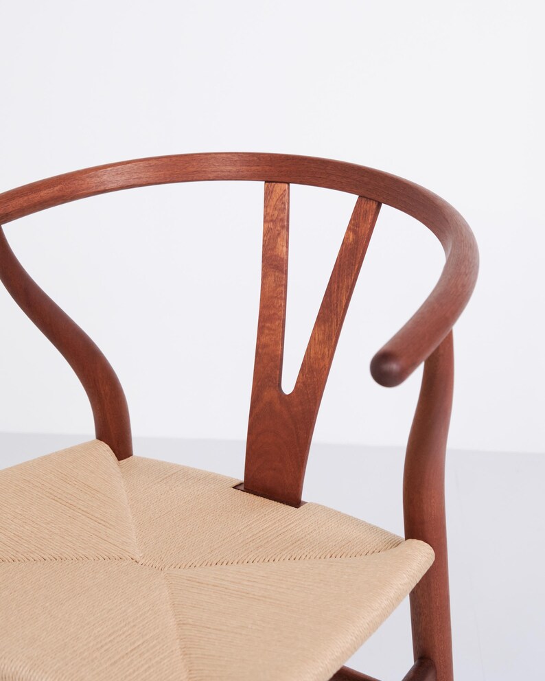 May include: Close-up of a wooden chair with a curved back and woven seat. The chair's frame is a rich brown color, and the seat is a light beige. The back of the chair has a distinctive Y-shaped design.