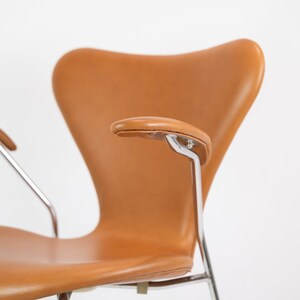 Puede incluir: Una silla de cuero marr&oacute;n con patas y brazos cromados. La silla tiene un respaldo curvo y un asiento c&oacute;modo.