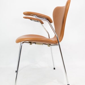 Puede incluir: Una silla de cuero marr&oacute;n con patas y brazos cromados. La silla tiene un respaldo curvo y un asiento c&oacute;modo.