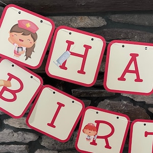 May include: A pink and white banner with the words "Happy Birthday" spelled out. Each letter is on a separate card with a red border. The cards feature illustrations of a nurse, a bandage, a syringe, and a heart.