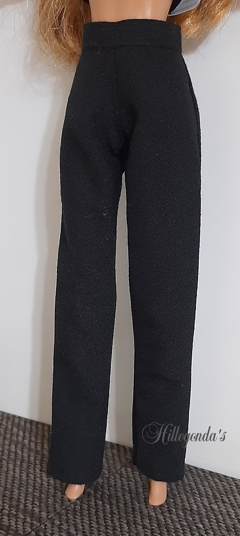 Puede incluir: Pantalones negros para una mu&ntilde;eca. Los pantalones est&aacute;n hechos de una tela texturizada y tienen una pierna recta.
