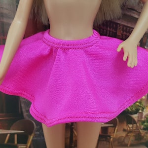 May include: A bright pink mini skirt with a ruffled hem and a simple design. The skirt is made of a soft, stretchy fabric.