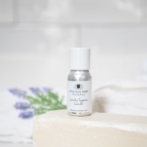 Puede incluir: Una peque&ntilde;a botella plateada con tapa blanca, etiquetada "Little Beau Sheep Naturally British Laundry Fragrance Lavender". La botella est&aacute; sobre una pastilla de jab&oacute;n blanca, con una rama de lavanda en el fondo.