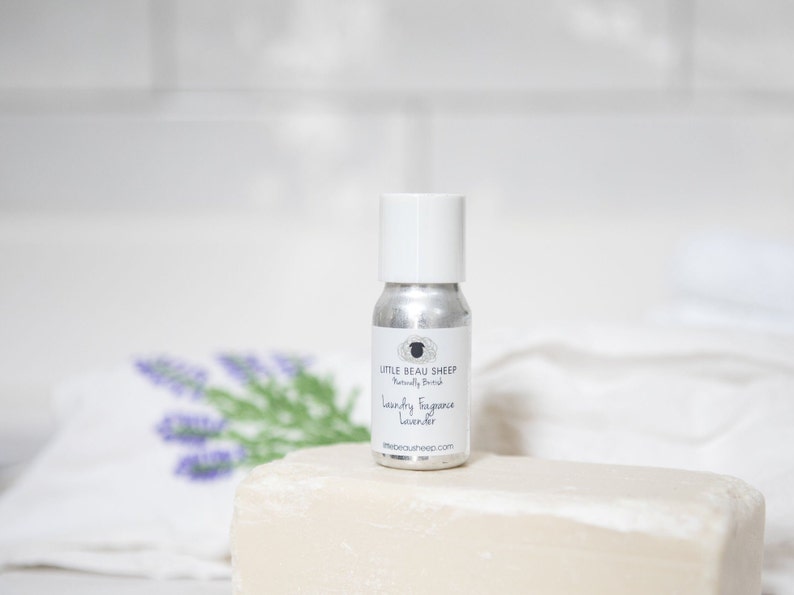 Puede incluir: Una peque&ntilde;a botella plateada con tapa blanca, etiquetada "Little Beau Sheep Naturally British Laundry Fragrance Lavender". La botella est&aacute; sobre una pastilla de jab&oacute;n blanca, con una rama de lavanda en el fondo.