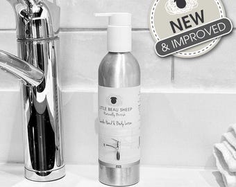 May include: A silver hand and body lotion bottle with a white pump dispenser. The label reads "Little Beau Sheep Naturally British Hand & Body Lotion". A "New & Improved" sticker is in the background. The lotion bottle is next to a chrome faucet.
