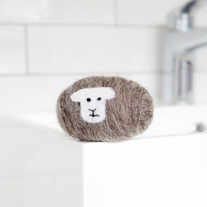 Puede incluir: Una oveja de fieltro de lana marrón con la cara blanca, sentada sobre una superficie blanca.