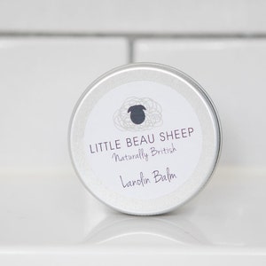 May include: A silver tin of Lanolin Balm with a white label. The label has a black sheep logo and reads "LITTLE BEAU SHEEP Naturally British Lanolin Balm". The tin is on a white surface.