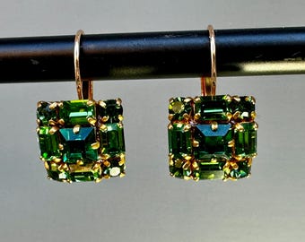 May include: A pair of gold earrings with a square design featuring a cluster of green gemstones.