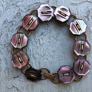 May include: A bracelet made of iridescent purple and brown buttons connected by gold-toned metal links.