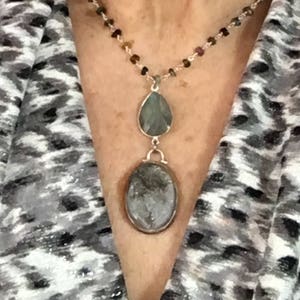 May include: A silver chain necklace with a teardrop-shaped pendant and a round pendant, both with green and gray stones.