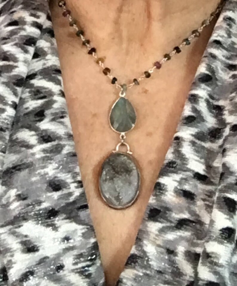 May include: A silver chain necklace with a teardrop-shaped pendant and a round pendant, both with green and gray stones.