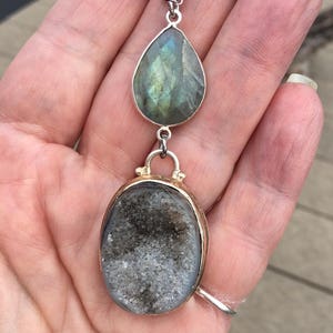 May include: A silver chain necklace with a teardrop-shaped labradorite gemstone pendant and a round, gray agate pendant.