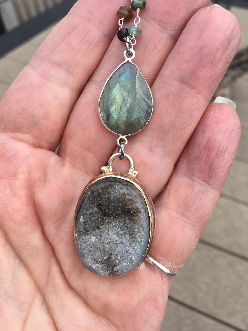 May include: A silver chain necklace with a teardrop-shaped labradorite gemstone pendant and a round, gray agate pendant.