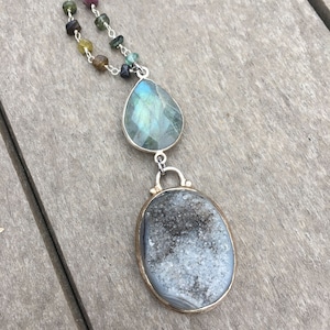 May include: A silver chain necklace with a teardrop-shaped labradorite gemstone pendant and a larger oval-shaped agate pendant with a silver setting.
