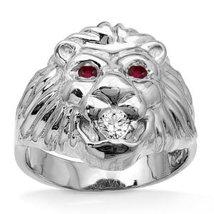 May include: A silver lion head ring with ruby eyes and a diamond in its mouth. The ring has a detailed mane and a polished finish, showcasing a bold and regal design. The ring is a statement piece.