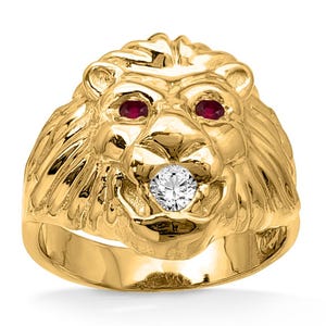 Könnte beinhalten: Ein goldfarbener Löwenring mit Rubinaugen und einem Diamanten im Maul. Der Ring ist eine detaillierte Skulptur eines Löwenkopfes, die Mähne und Gesichtszüge zeigt. Ein auffälliges Schmuckstück.