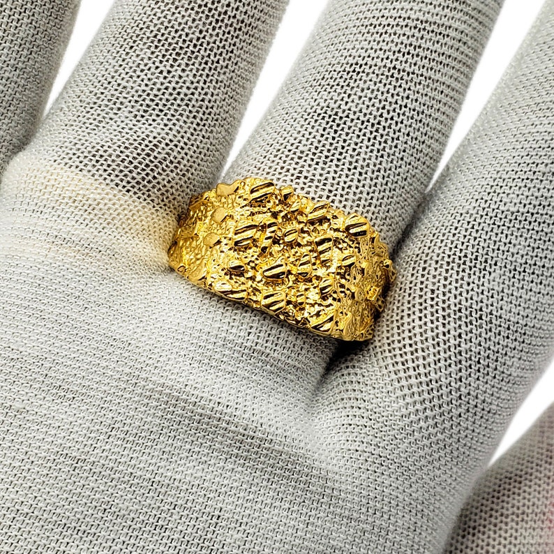 May include: A gold ring with a textured surface. The ring is wide and has a chunky design.