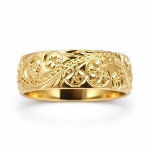 May include: A polished yellow gold band ring featuring an intricate, deeply engraved floral and scroll pattern that wraps around the entire exterior surface, creating a textured, reflective finish with detailed leaf and petal motifs.