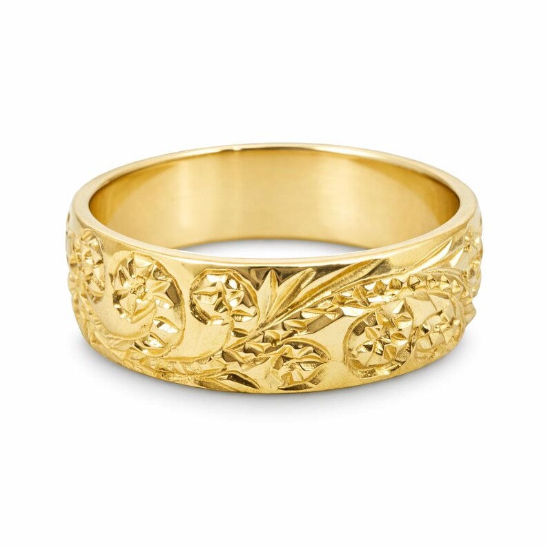 May include: A polished yellow gold band ring featuring an intricate, continuous engraved pattern of stylized floral motifs and swirling leaves that wrap around the entire outer surface of the metal band with a bright, reflective finish.