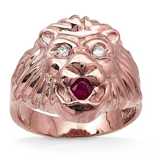 May include: Rose gold lion ring with diamond accents for eyes and a ruby for the mouth. The ring features a detailed lion's head design, showcasing the mane and facial features. A statement piece of jewelry.