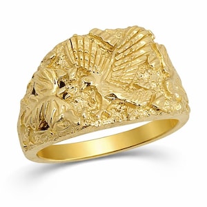May include: A yellow gold ring featuring a textured, nugget-style surface with a raised, detailed eagle motif in flight. The band is smooth and polished on the interior, while the exterior showcases a rugged, organic relief design.