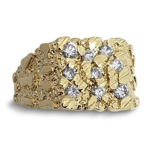 May include: A gold ring featuring a textured nugget-style surface with a wide band. The ring is set with eight round, clear, faceted stones arranged in a grid pattern across the top, showcasing a metallic yellow finish and reflective surfaces.