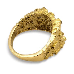 May include: A gold ring featuring a textured, nugget-style surface across the band and the top section. The metal has a polished, reflective finish with irregular, raised bumps and indentations that create a rugged, organic appearance throughout.