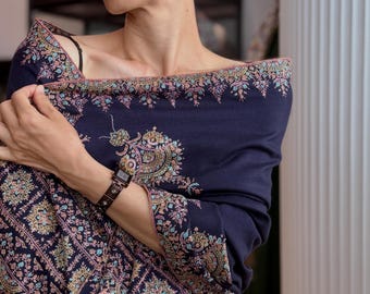 May include: A dark navy blue shawl featuring intricate, multi-colored floral embroidery along the edges and across the fabric. The embroidery includes delicate patterns in shades of pink, light blue, and gold, creating a detailed border design.