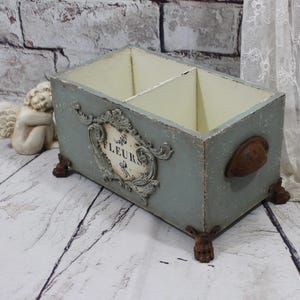 May include: A distressed blue wooden box with two compartments, ornate embellishments, and a handle. The box has decorative feet and a label reading "FLEURS".