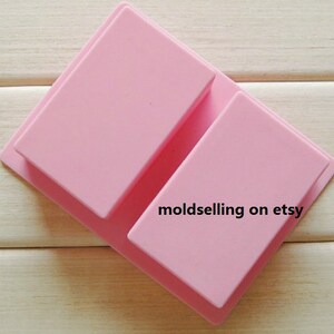 May include: Two pink silicone moulds for making rectangular bars of soap. The moulds are stacked on top of each other. The text "moldselling on etsy" is printed on the bottom mould.