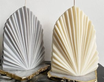 May include: Two decorative candles shaped like a fan, one in grey and one in cream, on a white marble base with gold accents.