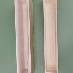 Könnte beinhalten: Eine rechteckige Holzform mit einem weißen Silikoneinsatz und eine separate, leere rechteckige Holzform. Beide Gegenstände sind lang, schmal und aus hellem Holz mit sichtbarer Maserung gefertigt und für handwerkliche Zwecke konzipiert.