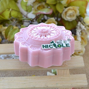 Pu&ograve; includere: Un sapone rosa a forma di fiore con un design decorativo e la parola "NICOLE" in lettere verdi. Il sapone ha un centro rialzato.