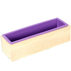 May include: A wooden soap mold with a purple silicone insert. The mold is made of natural wood and has a light brown color.