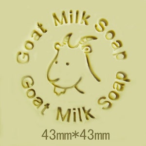 Puede incluir: Una barra de jabón de leche de cabra amarilla con un diseño de cabeza de cabra y el texto "Goat Milk Soap" en un círculo alrededor de la cabra. El jabón mide 43 mm por 43 mm.