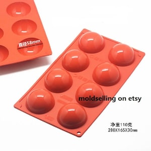 May include: A red silicone mold with six round cavities for making spherical candies or chocolates. The mold measures 280x165x30mm and has a diameter of 58mm.