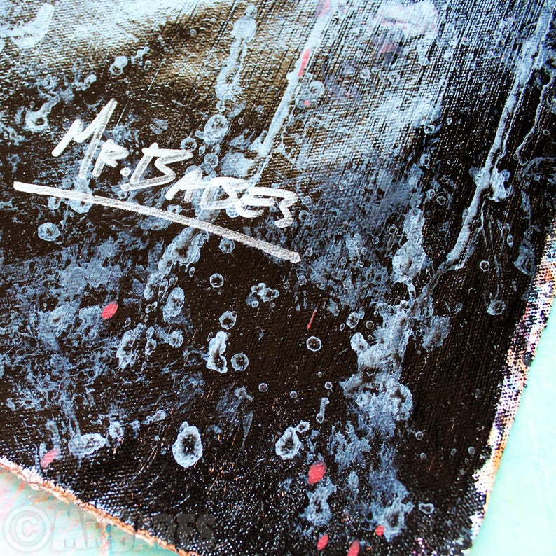 May include: Close-up of a black canvas with white paint splatters and the signature "Mr. Isaksen" in white paint.