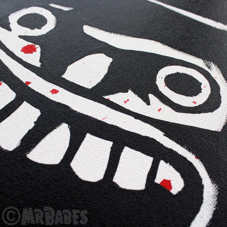 May include: Black canvas tote bag with a white graphic of a smiling face with large teeth and eyes. The graphic has red paint splatters.