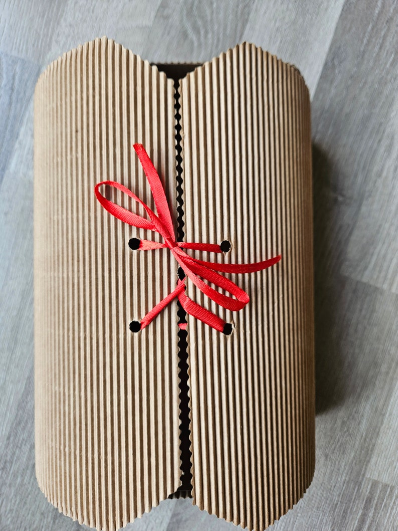 May include: A brown cardboard box with a red ribbon tied around it. The box has a corrugated texture and is tied with a bow.