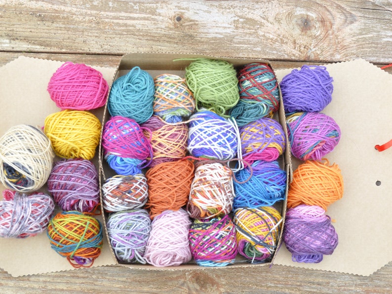 May include: A box filled with colorful yarn balls in various shades of pink, purple, blue, green, orange, yellow, and white. The yarn is arranged in a grid pattern.