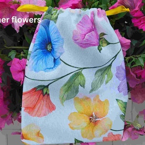 May include: A white drawstring bag with a floral print featuring blue, pink, yellow, and orange flowers. The bag has a yellow drawstring.