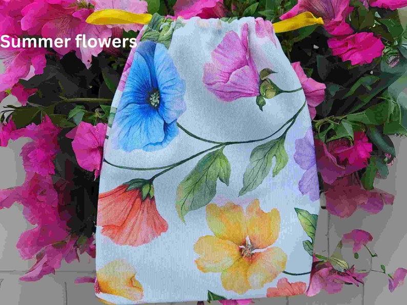 May include: A white drawstring bag with a floral print featuring blue, pink, yellow, and orange flowers. The bag has a yellow drawstring.