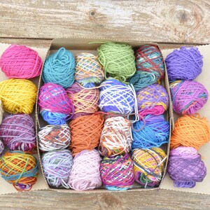 May include: A box filled with colorful yarn balls in various shades of pink, purple, blue, green, orange, yellow, and white. The yarn is arranged in a grid pattern.