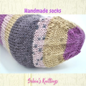 Puede incluir: Primer plano de un calcet&iacute;n hecho a mano con rayas de hilo morado, rosa, marr&oacute;n y gris. El calcet&iacute;n est&aacute; tejido con un patr&oacute;n texturizado. El texto "Handmade socks" est&aacute; en la parte superior de la imagen y "Solvia's Knittings" en la parte inferior.