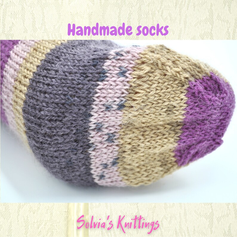 Puede incluir: Primer plano de un calcet&iacute;n hecho a mano con rayas de hilo morado, rosa, marr&oacute;n y gris. El calcet&iacute;n est&aacute; tejido con un patr&oacute;n texturizado. El texto "Handmade socks" est&aacute; en la parte superior de la imagen y "Solvia's Knittings" en la parte inferior.