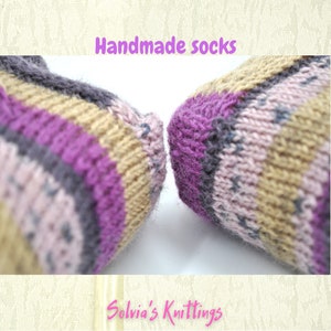 Puede incluir: Primer plano de un par de calcetines hechos a mano con un patr&oacute;n a rayas en tonos rosa, morado, gris y beige. Los calcetines est&aacute;n tejidos y tienen una textura suave y peluda.