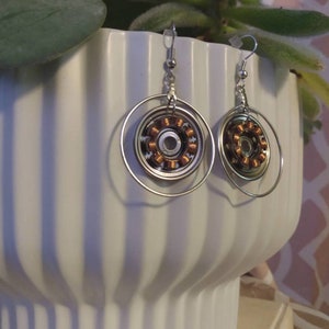 May include: A pair of silver earrings with a circular design. Each earring features a copper-colored coil in the center, surrounded by a silver ring.